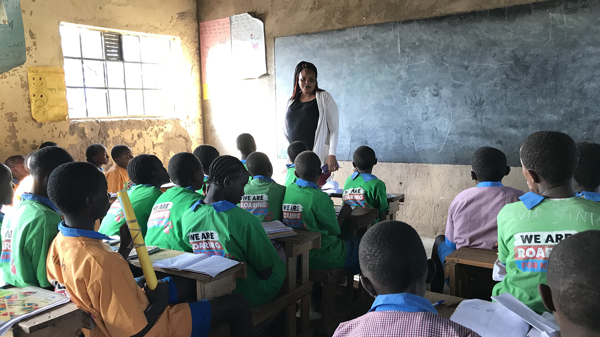 A class full of Kenyan school children wearing green Born Free t-shirts, looking at a teacher in front of a chalk board