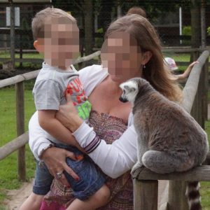 A lady holding a young child close-up to a lemur. The people's faces are blurred
