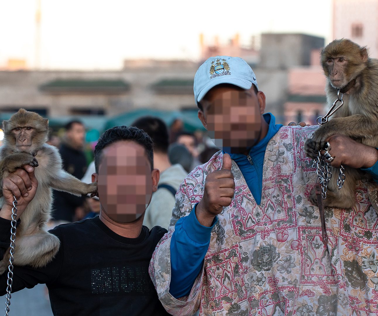 Two men with blurred faces posing with macaques on chains